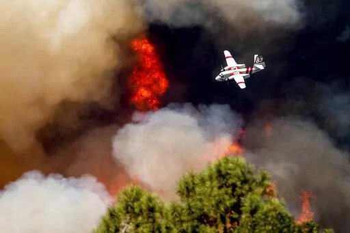 An air tanker flies past flames while battling the Oak Fire in Mariposa County, Calif., Sunday, July 24, 2022. Wildfires, floods and soaring temperatures have made climate change real to many Americans. Yet a sizeable number continue to dismiss the scientific consensus that human activity is to blame. That's in part because of a decades-long campaign by fossil fuel companies to muddy the facts and promote fringe explanations. (AP Photo/Noah Berger, File)