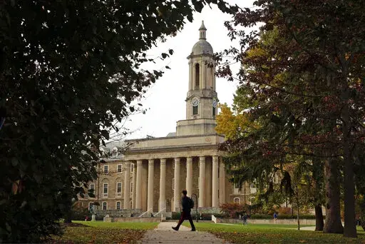 FILE- People walk by Old Main on the Penn State University main campus on Nov. 9, 2017 in State College, Pa. Applying to college is rarely easy, but applicants in 2022 are faced with one additional challenge: creating a compelling college application after nearly two years of disruptions as a result of the pandemic.   (AP Photo/Gene J. Puskar, File)