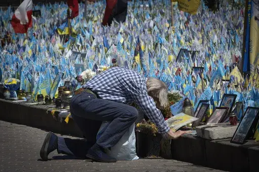 A man kneels in front of a makeshift memorial for fallen Ukrainian soldiers on Independence Square in Kyiv, Ukraine, Tuesday, July 23, 2024. Each flag brought by relatives bears a name of a soldier killed in battle with Russian troops. (AP Photo/Efrem Lukatsky)