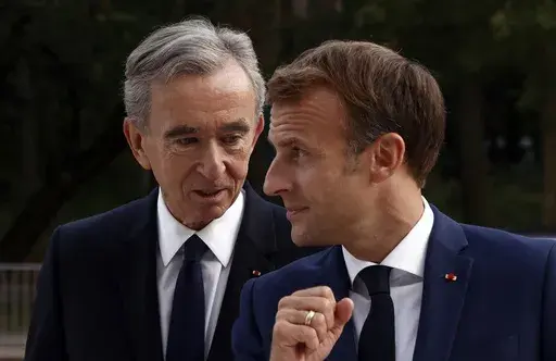 LVMH luxury group CEO Bernard Arnault, left, and French President Emmanuel Macron arrive at Fondation Louis Vuitton to visit the exhibition 'The Morozov Collection, Icons of Modern Art' in Paris, Tuesday, Sept. 21, 2021. With a major sponsorship role aimed at burnishing the image of the Paris 2024 Summer Olympic Games and the French capital, it's a new chapter in LVMH's specialty of selling exclusivity at a grand scale under its chair and CEO, Arnault. (Yoan Valat/Pool Photo via AP, File)