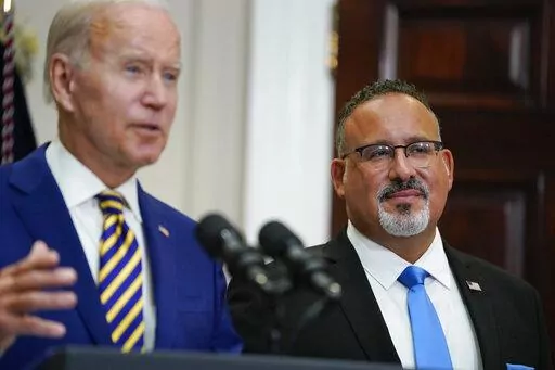 Education Secretary Miguel Cardona listens as President Joe Biden speaks about student loan debt forgiveness in the Roosevelt Room of the White House, Wednesday, Aug. 24, 2022, in Washington. (AP Photo/Evan Vucci)