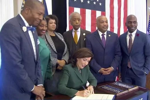 CORRECTS CITY TO NEW YORK - This image from video provided by the Office of The Governor shows New York Gov. Kathy Hochul signing a bill in New York, Tuesday, Dec. 19, 2023, to create a commission tasked with considering reparations to address the persistent, harmful effects of slavery in the state. She is joined by, standing from left: Dr. Yohuru Williams, Founding Director of the Racial Justice Initiative at the University of St. Thomas; Andrea Stewart-Cousins, Majority Leader of the NY State 