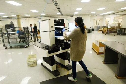 A Maricopa County election worker places ballots in the ballot counting machine after Arizona's primary election Wednesday, Aug. 3, 2022, in Phoenix. (AP Photo/Ross D. Franklin)