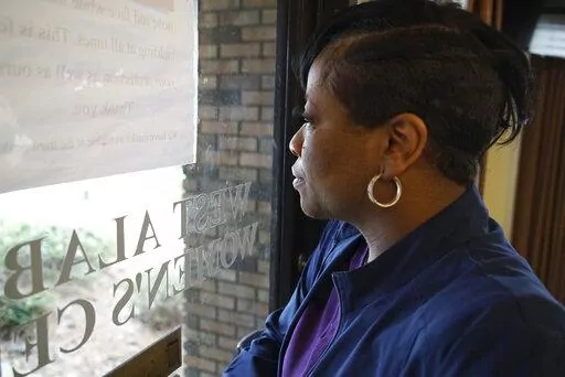 Alesia Horton, director of the West Alabama Women's Center in Tuscaloosa, Ala., looks out the window at protesters on Tuesday, March 15, 2022. A deeply religious woman, she says of those who picket the clinic: "God isn't theirs. God is all of ours." (AP Photo/Allen G. Breed)