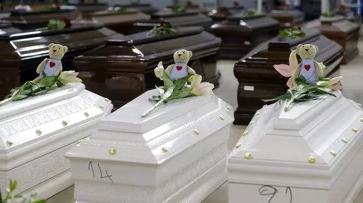 Teddy bears and flowers placed are placed on the coffins of deceased migrants inside a hangar at Lampedusa's airport, Italy, Saturday, Oct. 5, 2013. A decade ago this year, the head of the EU's executive branch, Jose Manuel Barroso stood visibly shaken before hundreds of coffins holding the corpses of migrants drowned off the Italian Island of Lampedusa. (AP Photo/Luca Bruno, File)