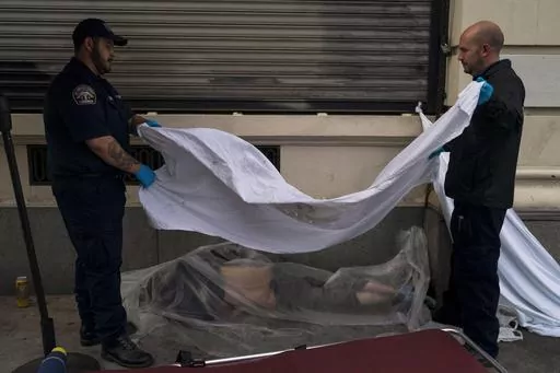 Forensic assistant Laurentiu Bigu, left, and investigator Ryan Parraz from the Los Angeles County coroner's office cover the body of a homeless man found dead on a sidewalk in Los Angeles on April 18, 2022. The 60-year-old man died from the effects of methamphetamine, according to his autopsy report. Drug overdose deaths in the U.S. went up slightly in 2022 after two big leaps during the pandemic. (AP Photo/Jae C. Hong, File)