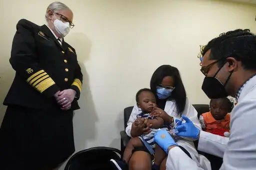 Pediatrician Emy Jean-Marie, center, holds her nine-month-old son Adedeji Adebayo, Emiola Adebayo, 3, on her lap as Dr. Nizar Dowla, right, administers a vaccine while        Department of Health and Human Services Assistant Secretary for Health, Admiral Rachel Levine, left, looks on, Tuesday, June 28, 2022, at the Borinquen Health Care Center in Miami. Florida is the only state that didn't pre-order the under-5 vaccine, and state Surgeon General Joseph Ladapo has recommended against vacci