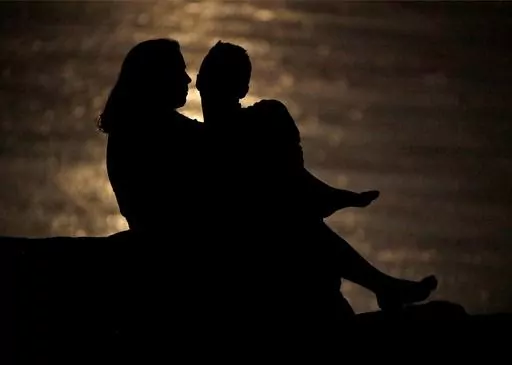 In this June 27, 2018, file photo a couple is silhouetted against moonlight reflecting off the Missouri River as they watch the full moon rise beyond downtown buildings in Kansas City, Mo. Money can create stress within a relationship, but talking through expectations and money beliefs can help couples get on the same page. In fact, conflict over money can be healthy, partly because we often partner with people who are our financial opposites. (AP Photo/Charlie Riedel, File)