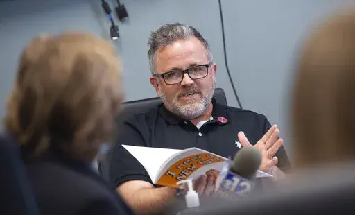 Toby Price, a former assistant principal at Gary Road Elementary School in Byram, Miss., testifies during an appeal hearing at the Hinds County Schools administration building in Raymond, Miss., Monday, March 28, 2022, regarding his dismissal after reading the children's book he's holding, "I Need a New Butt!" by Dawn McMillan. Price told the Clarion Ledger he received a 12-page order Monday, May 11, 2022, showing the Hinds County School Board had voted 2-1 to uphold the superintendent's decisio