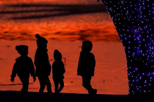 In this Dec. 26, 2020 file photo, children are silhouetted against a pond as they look at Christmas lights at a park in Lenexa, Kan. Custodial accounts are a way to invest for minors and give them a headstart on building wealth. How can you ensure they’re financially responsible enough to manage their assets when they reach the age of majority? One way is to share your money values with them and teach budgeting basics as well as saving tactics early on. (AP Photo/Charlie Riedel, File)