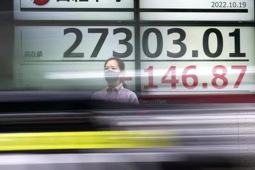 A person wearing a protective mask stands in front of an electronic stock board showing Japan's Nikkei 225 index as a vehicle passing by at a securities firm Wednesday, Oct. 19, 2022, in Tokyo. Asian stock markets were mixed Wednesday after Wall Street rose on strong corporate profit reports. (AP Photo/Eugene Hoshiko)
