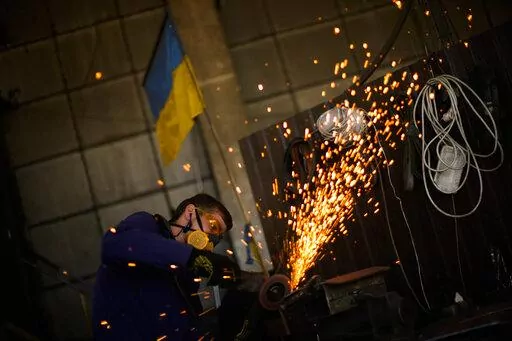 A volunteer shapes metal plates with an angle grinder at a facility producing material for Ukrainian soldiers in Zaporizhzhia, Ukraine, Saturday, May 7, 2022. An old industrial complex in the southeastern Ukrainian riverside city of Zaporizhzhia has become a hive of activity for volunteers producing everything from body armor to camouflage nets, anti-tank obstacles to heating stoves and rifle slings for Ukrainian soldiers fighting the Russian invasion. (AP Photo/Francisco Seco)