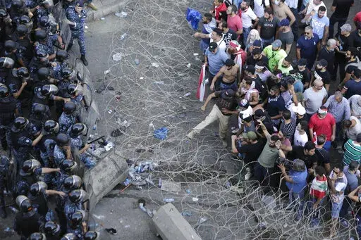 FILE- Riot police stand guard as anti-government protesters try to remove a barbed-wire barrier to advance towards the government buildings during a protest against a slate of new proposed taxes, including a $6 monthly fee for using Whatsapp voice calls, in Beirut, Lebanon, Saturday, Oct. 19, 2019. The measures set a spark to long smoldering anger against the ruling class and months of mass protests. Irregular capital controls were put in place, cutting people off from their savings as the curre