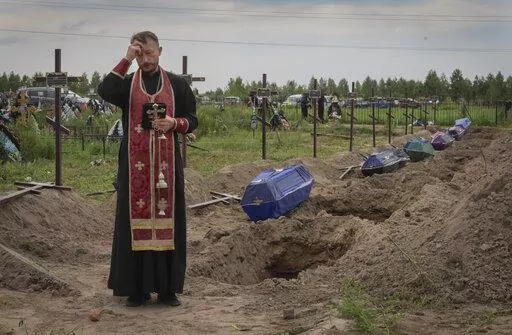A priest prays for unidentified civilians killed by Russian troops during Russian occupation in Bucha, on the outskirts of Kyiv, Ukraine, Thursday, Aug. 11, 2022. Eleven unidentified bodies exhumed from a mass grave were buried in Bucha Thursday (AP Photo/Efrem Lukatsky)