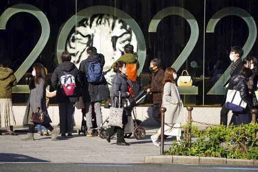 People wearing protective masks to help curb the spread of the coronavirus stand outside a window displaying a 2022 New Year celebration along a street Wednesday, Dec. 29, 2021, in Tokyo. (AP Photo/Eugene Hoshiko)