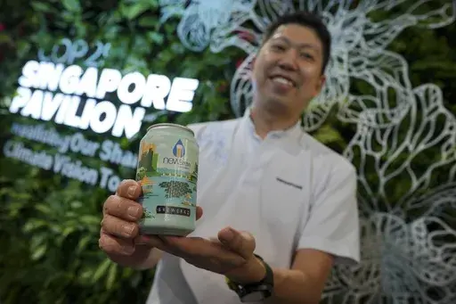 Nick Chow, part of the COP29 Singapore Pavilion team, poses for a photo with NEWBrew, beer made with treated wastewater, during the COP29 U.N. Climate Summit, Friday, Nov. 15, 2024, in Baku, Azerbaijan. (AP Photo/Peter Dejong)