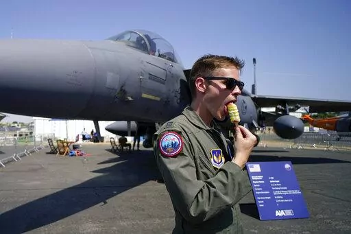A member of the military personnel eats an ice cream as he stands past an F15E Strike Eagle fighter jet, on display at the Farnborough Air Show fair in Farnborough, England, Tuesday, July 19, 2022. The future for fighter pilots was on display at the Farnborough International Airshow near London, one of the world’s biggest aviation, defense and aerospace expos. New technologies take on a bigger role in the cockpit, redefining what it means to be a ''Top Gun''. (AP Photo/Alberto Pezzali, File)