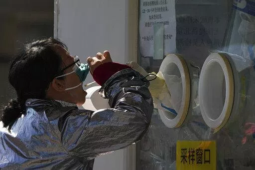A woman pulls her face mask to get her routine COVID-19 throat swab at a coronavirus testing site in Beijing, Thursday, Oct. 6, 2022. Sprawling Xinjiang is the latest Chinese region to be hit with sweeping COVID-19 travel restrictions, as China further ratchets up control measures ahead of a key Communist Party congress later this month. (AP Photo/Andy Wong)