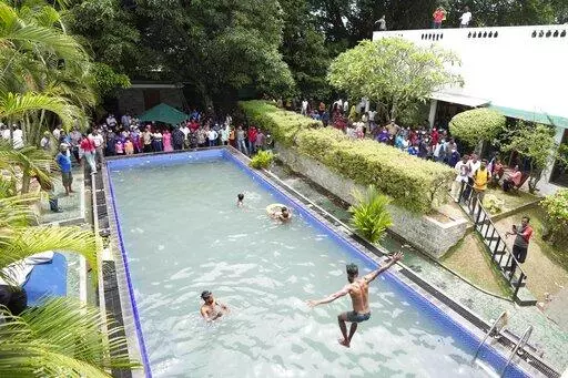 Protesters swim as onlookers wait at a swimming pool in president's official residence a day after it was stormed in Colombo, Sri Lanka, Sunday, July 10, 2022. Sri Lanka’s opposition political parties will meet Sunday to agree on a new government a day after the country’s president and prime minister offered to resign in the country’s most chaotic day in months of political turmoil, with protesters storming both officials’ homes and setting fire to one of the buildings in a rage over the