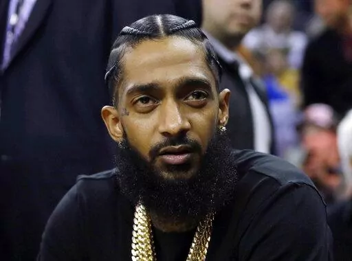 Rapper Nipsey Hussle attends an NBA basketball game between the Golden State Warriors and the Milwaukee Bucks in Oakland, Calif., March 29, 2018. Three years after rapper Hussle was gunned down outside a Los Angeles clothing store that he founded to help revitalize the neighborhood where he grew up, a trial will finally begin Wednesday, June 15, 2022, for the man charged with killing him. (AP Photo/Marcio Jose Sanchez, File)