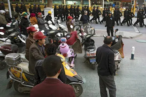 Residents watch a convoy of security personnel armed with batons and shields patrol through central Kashgar in western China's Xinjiang region, Nov. 5, 2017. China's discriminatory detention of Uyghurs and other mostly Muslim ethnic groups in the western region of Xinjiang may constitute crimes against humanity, the U.N. human rights office said in a long-awaited report Wednesday, Aug. 31, 2022, which cited "serious" rights violations and patterns of torture in recent years. (AP Photo/Ng Han Gua