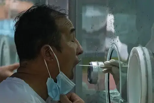 A man pulls his mask to get his routine COVID-19 throat swab at a coronavirus testing site in Beijing, Tuesday, Aug. 9, 2022. Chinese authorities have closed Tibet's famed Potala Palace after a minor outbreak of COVID-19 was reported in the Himalayan region. (AP Photo/Andy Wong)