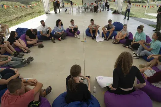 First lady Olena Zelenska, centre in white, talks with children during her visit to the rehabilitation camp for children affected by war, organized by the Voices of Children charity foundation and financially supported by the Olena Zelenska Foundation in Uzhhorod, Ukraine, Tuesday, Aug. 27, 2024. (AP Photo/Efrem Lukatsky)