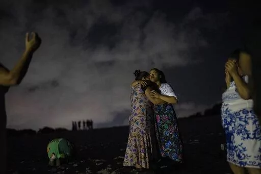 Mag Oliveira embraces her daughter Najla as they pray in an area of the Abaete dune system, on a steep rise of sand evangelicals have come to call the "Holy Mountain", in Salvador, Brazil, late Friday night, Sept. 16, 2022. Evangelicals have been converging on the dunes for some 25 years but especially lately, with thousands now coming each week to sing, pray and enter trancelike states to commune with God.(AP Photo/Rodrigo Abd)