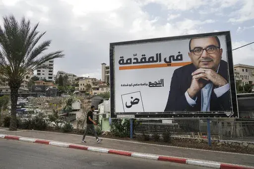 A man walks by an election campaign billboard showing Sami Abu Shehadeh, head of the nationalist Balad party, in the northern Israeli city of Umm al-Fahm, Friday, Oct. 21, 2022.  Israel’s Palestinian citizens, a minority whose voice is often drowned out, delegitimized or disparaged in Israel’s noisy politics, could hold the key to breaking the country’s political deadlock. Israel heads to the polls Nov. 1 for the fifth time in less than four years. (AP Photo/Mahmoud Illean)