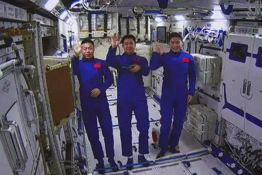 In this photo released by Xinhua News Agency, an image taken off the screen at the Beijing Aerospace Control Center shows Chinese astronauts from left, Cai Xuzhe, Chen Dong and Liu Yang wave from inside the Wentian lab module on Monday, July 25, 2022. China added the laboratory to its permanent orbiting space station Monday as it moves toward completing the structure in coming months. (Guo Zhongzheng/Xinhua via AP)