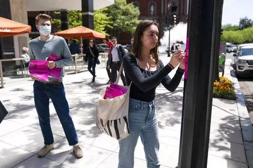 George Washington University student Kai Nilsen, left, watches as American University student Magnolia Mead as they put up posters near the White House promoting student loan debt forgiveness, Friday, April 29, 2022, in Washington. (AP Photo/Evan Vucci)