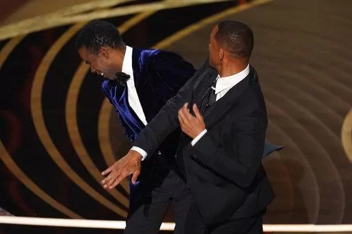 Will Smith, right, hits presenter Chris Rock on stage while presenting the award for best documentary feature at the Oscars on Sunday, March 27, 2022, at the Dolby Theatre in Los Angeles. Rock will be the first artist to perform on Netflix's first-ever live, global streaming event. (AP Photo/Chris Pizzello, File)