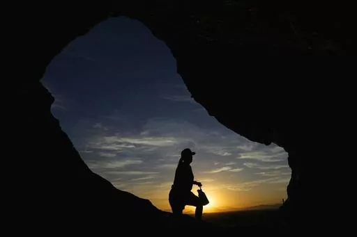 A hiker walks past the Hole-in-the-Rock at Papago Park during sunrise July 17, 2023, in Phoenix. Scientists say by far the biggest cause of the recent extreme warming is human-caused climate change and a natural El Nino. But some say there’s got to be something more. (AP Photo/Ross D. Franklin, File)