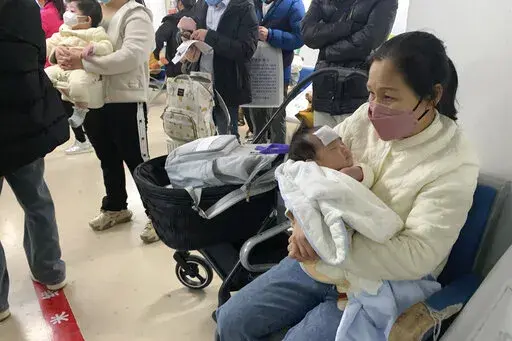 A woman tends to a child at the fever clinic of a Children's hospital in Beijing, Wednesday, Dec. 14, 2022. China's National Health Commission scaled down its daily COVID-19 report starting Wednesday in response to a sharp decline in PCR testing since the government eased antivirus measures after daily cases hit record highs. (AP Photo/Dake Kang)