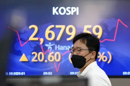 A currency trader walks by the screens showing the Korea Composite Stock Price Index (KOSPI) at a foreign exchange dealing room in Seoul, South Korea, Friday, June 3, 2022. Asian shares rose Friday amid mixed signs for investors such as rising energy prices and COVID-19 restrictions easing in China. (AP Photo/Lee Jin-man)