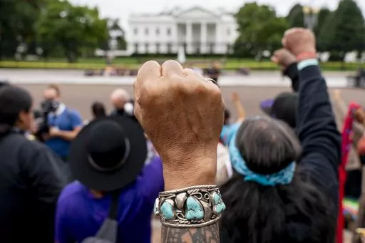 Wolf Ramerez of Houston, Texas, center, joins others with the Carrizo Comecrudo Tribe of Texas in holding up his fists as indigenous and environmental activists protest in front of the White House in Washington, Oct. 11, 2021. Members of the Native American Journalists Association are voting on whether to change the name to the Indigenous Journalists Association. (AP Photo/Andrew Harnik, file)