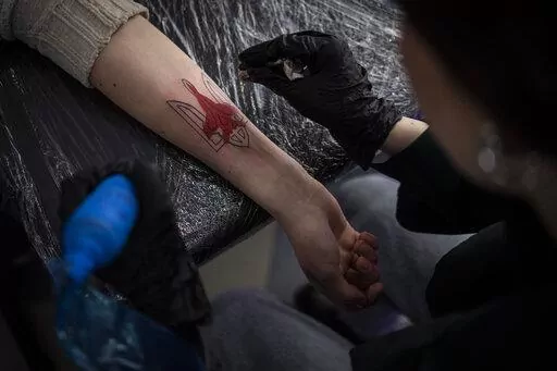 Ukrainian Natalia Tanchynets works on a patriotic-themed tattoo at her workshop in Lviv, Western Ukraine, Saturday, March 19, 2022. (AP Photo/Bernat Armangue)