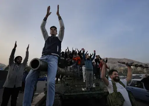 Syrian citizens stand on a government forces tank, that was left on a street, as they are celebrating during the second day of the take over of the city by the insurgents in Damascus, Syria, Monday, Dec. 9, 2024. (AP Photo/Hussein Malla)