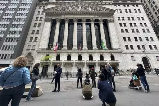 Tourists gather near the New York Stock Exchange on May 16, 2024, in New York. Shares retreated in Europe and Asia on Friday, May 24, 2024, after unexpectedly strong reports on the U.S. economy raised the possibility that interest rates may stay painfully high. (AP Photo/Peter Morgan, File)