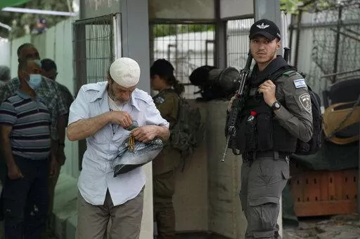 An Israeli Border Police officer secures a checkpoint from the West Bank town of Bethlehem into Jerusalem as a Palestinian man puts away his ID card while crossing for prayers during the Muslim holy month of Ramadan at the Al Aqsa mosque compound in Jerusalem's Old City, Friday, April 8, 2022. The apparent comeback of former Prime Minister Benjamin Netanyahu and the dramatic rise of his far-right and ultra-Orthodox allies in Israel's general election this week have prompted little more than shru