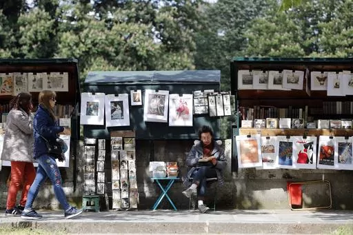 Visitors walk past a bookseller of used and antiquarian books called "Bouquiniste", in Paris, Thursday, May 10, 2018. French President Emmanuel Macron has revealed his bookish side and abandoned plans Tuesday, Feb. 13, 2024, to move the famed second-hand bookseller boxes flanking the banks of the Seine that are beloved by tourists, in preparation for July's Olympics opening ceremony in Paris. (AP Photo/Christophe Ena, File)