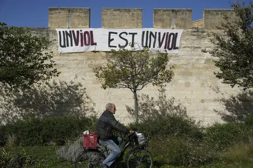 A man rides a bicycle in front of a banner reading: "A rape is a rape," in Avignon, southern France, on Oct. 16, 2024. (AP Photo/Lewis Joly, File)