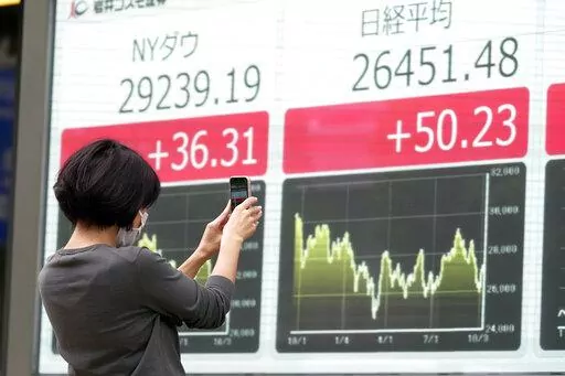 A person takes photos of an electronic stock board showing Japan's Nikkei and New York Dow indexes at a securities firm Wednesday, Oct. 12, 2022, in Tokyo. Asian shares were mostly lower on Wednesday following another volatile day on Wall Street, as traders braced for updates on inflation and corporate earnings. (AP Photo/Eugene Hoshiko)