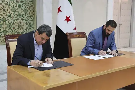 In this photo released by Syrian state news agency SANA, Syria's interim President Ahmad al-Sharaa, right, and Mazloum Abdi, the commander of the U.S.-backed Kurdish-led Syrian Democratic Forces, sign a deal in Damascus, Syria, Monday, March 10, 2025. (SANA via AP)