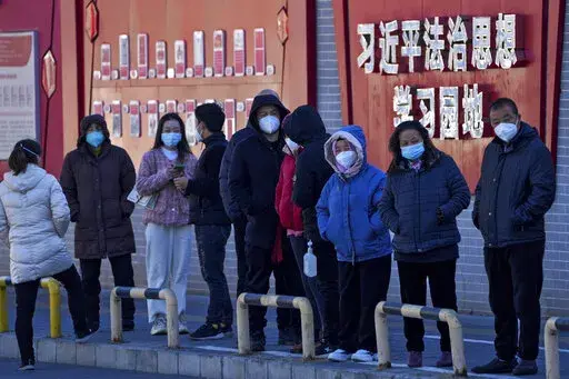 Residents wearing face masks line up for their routine COVID-19 tests along a wall displaying the words "Xi Jinping rule of law ideology learning ground" in Beijing, Monday, Dec. 5, 2022. China is easing some of the world's most stringent anti-virus controls and authorities say new variants are weaker. But they have yet to say when they might end a "zero-COVID" strategy that confines millions of people to their homes and set off protests and demands for President Xi Jinping to resign. (AP Photo/