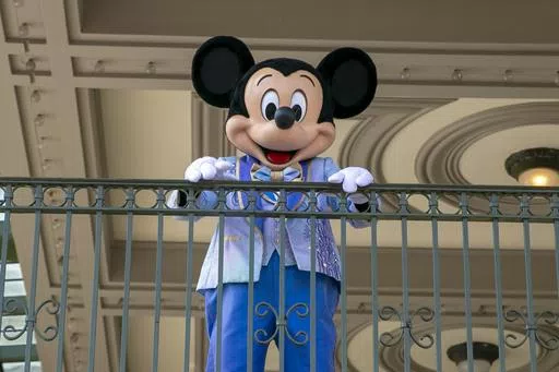 An actor dressed as Mickey Mouse greets visitors at the entrance to Magic Kingdom Park at Walt Disney World Resort, April 18, 2022, in Lake Buena Vista, Fla. Winnie the Pooh and Mickey Mouse have recently entered the public domain, making it possible for artists to use them freely. (AP Photo/Ted Shaffrey, File)