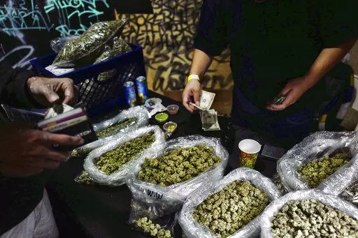 In this April 15, 2019, file photo, a vendor makes change for a marijuana customer at a cannabis marketplace in Los Angeles. An unwelcome trend is emerging in California, as the nation's most populous state enters its fifth year of broad legal marijuana sales. Industry experts say a growing number of license holders are secretly operating in the illegal market — working both sides of the economy to make ends meet. (AP Photo/Richard Vogel, File)