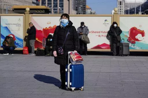 A traveler waits outside the Beijing railway station with her suitcase in Beijing, China, Friday, Jan. 28, 2022. The Beijing Winter Olympics is coinciding with the Chinese Lunar New Year and renewed Covid outbreaks prompting the Chinese authorities to call on the public to stay where they are instead of traveling to their hometowns for the year's most important family holiday. (AP Photo/Ng Han Guan)