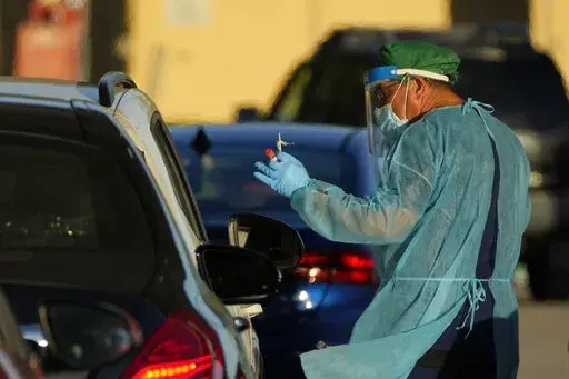 A health care worker tests people for COVID-19 at a drive-up testing center at Tropical Park, Wednesday, Dec. 29, 2021, in Miami. (AP Photo/Rebecca Blackwell)