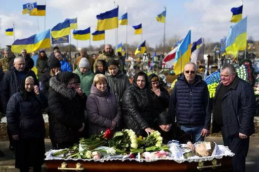Relatives gather next to the body of 29 year old Yana Rikhlitska, a Ukrainian army medic killed in the Bakhmut area, during the funeral in Vinnytsia, Ukraine, Tuesday, March 7, 2023. Just over a week ago, Yana Rikhlitska was filmed by The Associated Press as she helped treat wounded soldiers in a field hospital of Bakhmut area which has been pulverized as Russia presses a three-sided assault to seize it. (AP Photo/Thibault Camus)